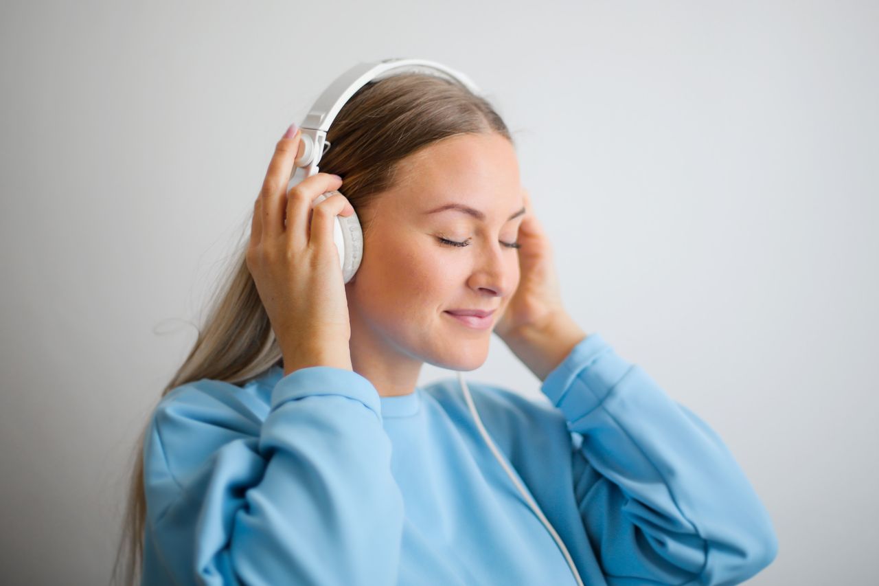 A serene young woman enjoying music with headphones on a neutral background.