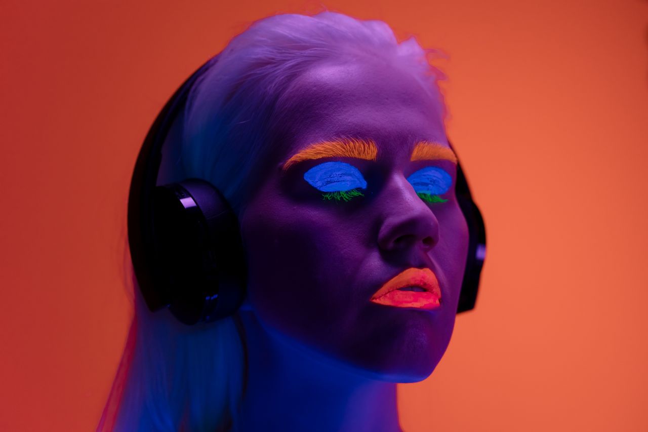 Colorful neon makeup portrait featuring a woman with headphones against a vibrant background.